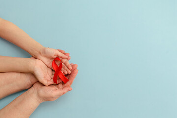 Concept of give blood transfusion and donation. Hands of mother and child hold red ribbon on blue background.Hemophilia day. World Health Day. Layout. Copy space. Banner. Mock up