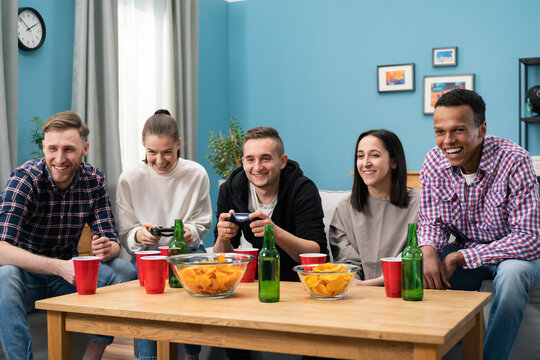 Excited friends playing video games at home, sitting on sofa and enjoying together. Cheerful mixed races friends resting in room sitting on couch playing video games using joystick. - Powered by Adobe