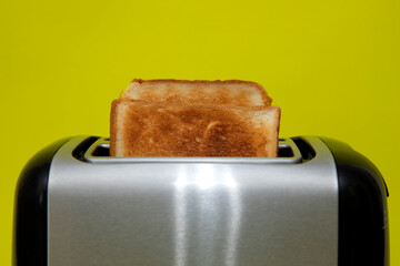 Grey toaster with hot toast on yellow background. Baked loaf with a delicious crust.