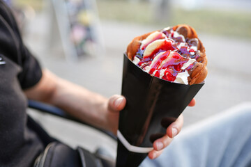 man holding takeaway waffles with ice cream, chocolate sauce and fresh fruits, natural dessert