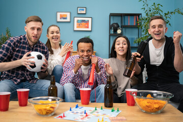 Happy diverse group of student sports fans throwing arms up in excitement celebrating goal watching sports event on TV together bonding as friends eating snacks drinking beer