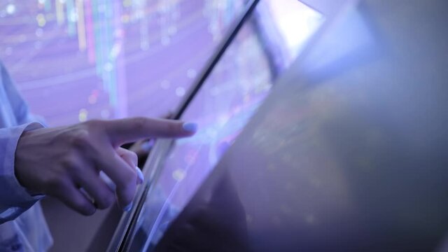 Woman using interactive touchscreen display of electronic multimedia kiosk in dark room of technology exhibition - scrolling and touching. Education, learning and technology concept