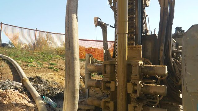 CLOSE UP: Close up shot of a massive hydraulic drill rig boring into the ground at a busy construction site. Heavy industrial machinery is drilling into the soil during geothermal pump installation.