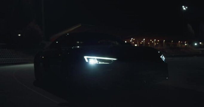 Cinematic close up shot of modern racing car with switched on headlights running on race track at night. Concept of passion for driving cars and engines,auto dealership, luxury cars, speed and power.