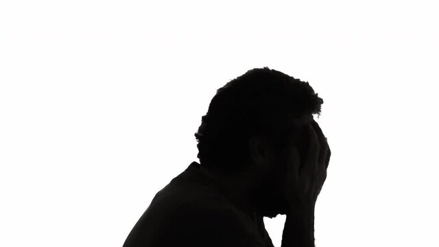 Silhouette black and white shot: a despairing man, covering his face with his hands, running away from burdensome problems.
