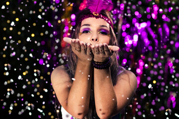 fashion portrait of beatiful woman dressed for carnival wearing colorful dress with colorful lights and confetti in background