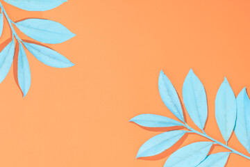 Minimal colorful tropical leaf flat lay idea. Exotic bright pastel blue leaves on vibrant orange background. Retro summer background concept with copy space.