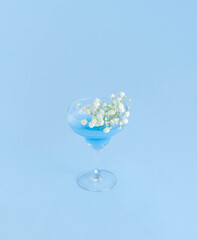 Minimal summer cocktail drink with white flowers and on bright sky blue background. Party life concept. Pale cold drink aeshetics. Copy space.