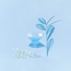 Minimal summer cocktail drink with white flowers and pastel blue tropical leaves on bright sky blue background. Party life concept. Modern cold drink aeshetics.