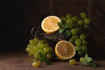 Still life with grapes, lemon and a tin vase on a brown stone background with blank space on the left. Dutch still life. Dark photo © Elena Sukhova
