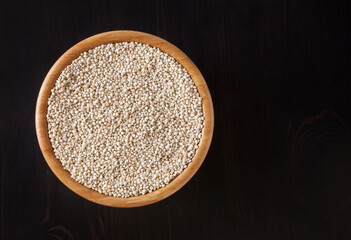 Dried white quinoa seeds in wooden bowl on black wooden background