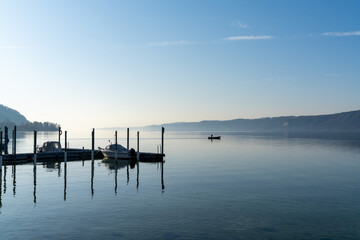 Fototapeta premium calm blue lake with moored ships and a small motorboat cruising through the water
