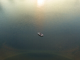 Fototapeta premium Fishing boat on the water in the rays of the sunset. Aerial drone view.