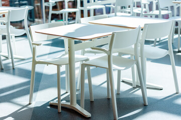 White tables and square-shaped chairs in the lighted dining room. Close up. Nobody