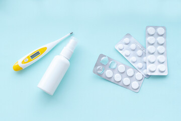 The medical thermometer and pills in blister packs on blue background. Disease prevention and...