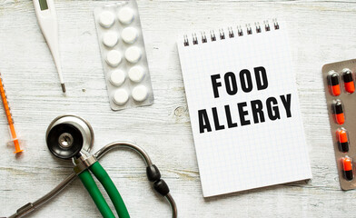 FOOD ALLERGY is written in a notebook on a white table next to pills and a stethoscope.