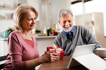 Obraz na płótnie Canvas Senior couple having video call. Happy husband giving his wife a gift..