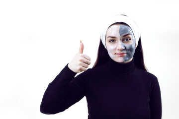 Woman doing cosmetic mask on a white background with place for text. A woman dressed in black and with a white headband at a beautician's appointment. Beautiful woman with a cosmetic mask on her face