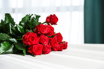 a bouquet of red roses on a table with a white tablecloth with sun glare 