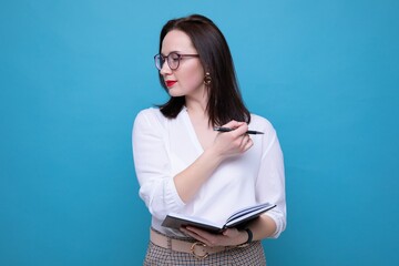 Young brunette woman with a diary and pen on a blue background