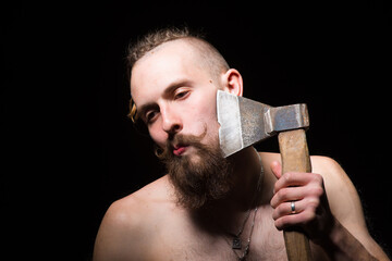 Young handsome man with bushy beard and large mustache shaves his beard with an old ax