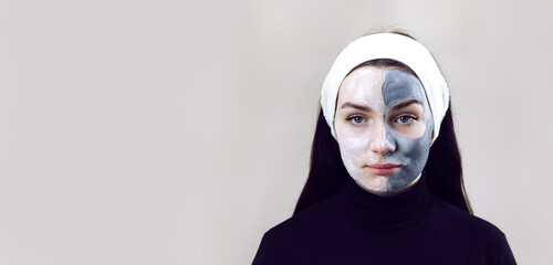 Woman doing cosmetic mask on a gray background with place for text. A woman dressed in black and with a white headband at a beautician's appointment. Beautiful woman with a cosmetic mask on her face