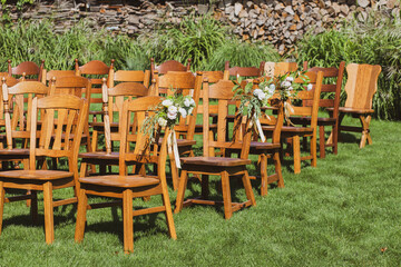 Many beautiful wooden chairs in the park. Wooden chairs decorated with wedding decor. Chairs for guests. Classic banquet chairs. Many chairs. Cermonia. Collection. Empty chairs for guests
