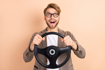 Fototapeta premium Photo of happy excited good mood crazy businessman riding car hold steering wheel isolated on beige color background