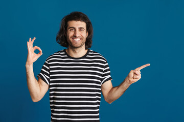 Smiling brunette man gesturing ok sign and pointing finger aside