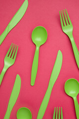 Green plastic forks, spoons, knifes on pink paper. Set of plastic cutlery in different spoons forks knives and eco-friendly plastic concept. Flat lay. Close-up.