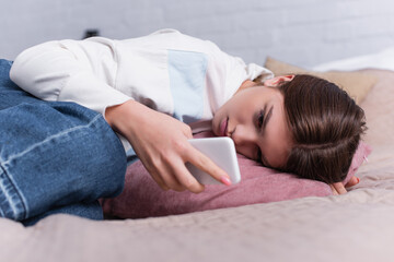 sad teenage girl lying on bed and using smartphone