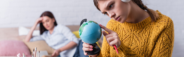sad teenage girl looking at globe with blurred mother on background, banner