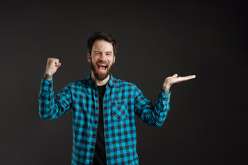 Bearded excited man in shirt making winner gesture and holding copyspace