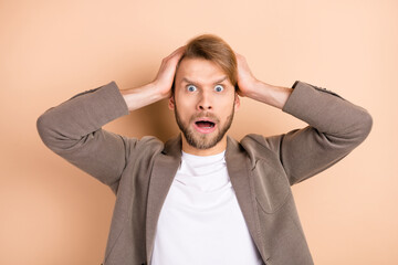 Photo of unhappy impressed young guy wear jacket arms head big eyes open mouth isolated beige color background