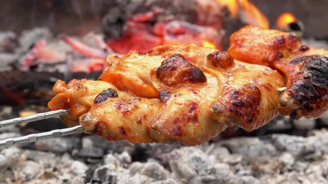 Close-up of delicious marinated chicken wings on the skewers frying above the open fire in rapid footage