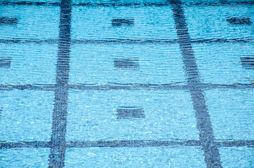 Fototapeta na wymiar Lined pool bottom through clear blue water. Clear swimming pool with transparent water. Water sports. Pool blue water background