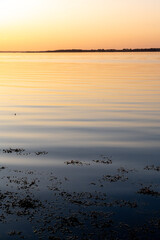 Smooth water surface to the horizon in soft dawn light with blue and orange colors.