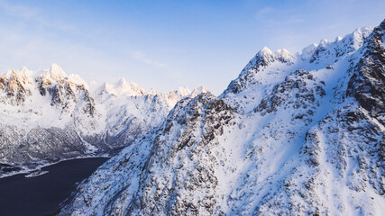 Fototapeta na wymiar Breathtaking bird's eye view of majestic fjord mountains covered with snow in winter. Aerial view of scenery rock peaks, picturesque beautiful nature landscape. Lofoten Island surrounds by Nordic sea