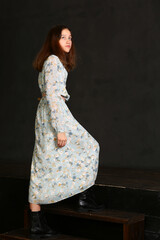 model girl in long printed dress and black boots full body portrait walking on dark wall background...