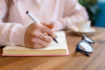 Close-up view of a woman`s hand with a pen, writes in a notebook