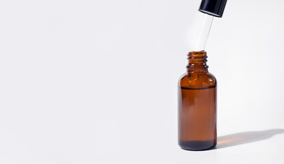 Cosmetic pipette with drops of oil or serum with shadow. Transparent brown bottle. Close up, copy space, banner. Grey background. Health, skin, body care. Aromatherapy.