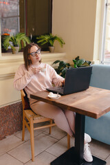 Woman drinks coffee and works at a laptop while sitting in a cafe