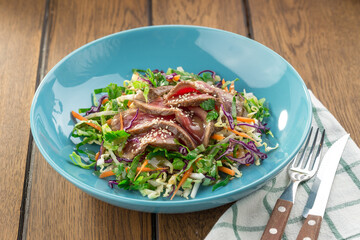 meat salad with roast beef, greens and sesame seeds asian style served on wooden table