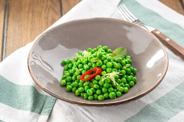 Plate of fresh green peas with chili pepper on the table close up