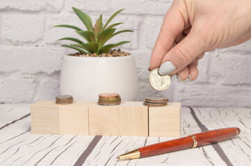 Front view of a cropped hand laying out coins letters on wooden cubes blocks on a light wooden table, investment concept