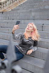 girl making a selfie with a mobile phone sitting on a grey staircase