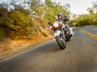 Motorcyclist dressed in leathers riding down a canyon street with trees blurred