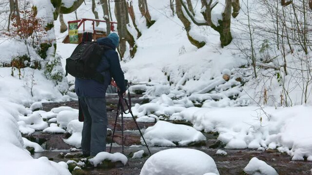 A man uses a camera to film a beautiful stream in a winter forest in the Carpathians