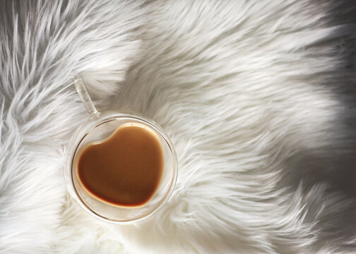 Close-up overhead view of a heart shaped cup of white coffee on a fluffy white rug