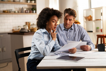 Young couple sitting in the kitchen preparing bills to pay. Stressed woman and man having financial problems.